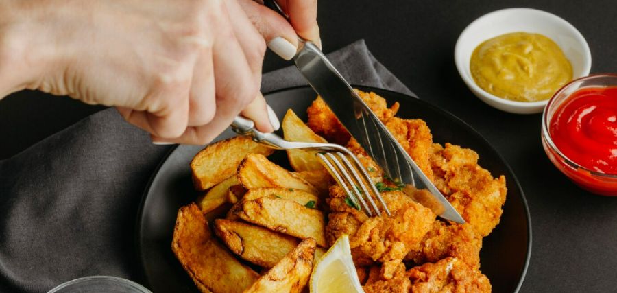 Pessoa comendo frango frito com batata rústica feitos na fritadeira elétrica sem óleo